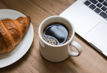 Чашка кофе с круасаном и ноутбуком на столе