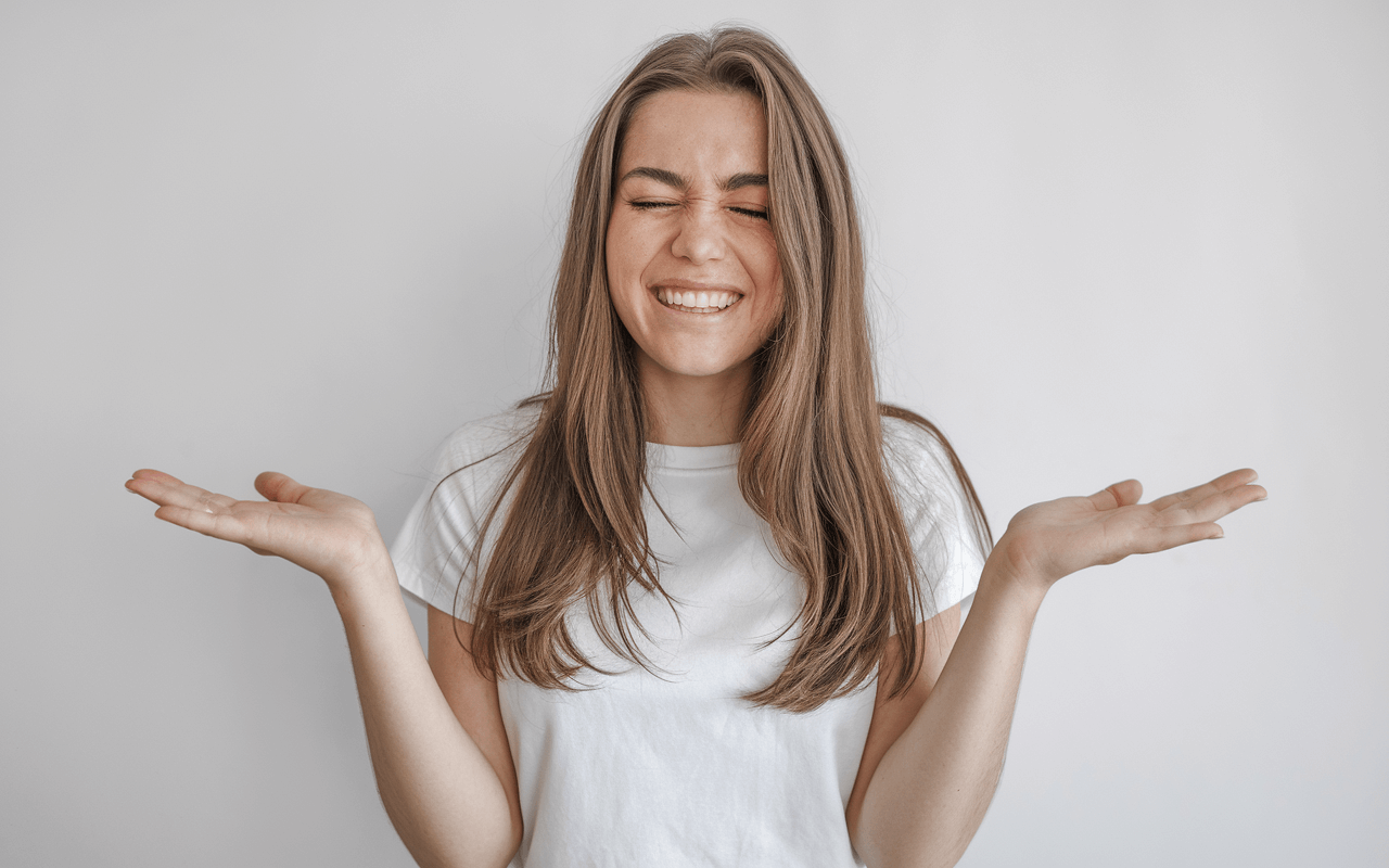 Дівчина ніяково радіє та розводить руки