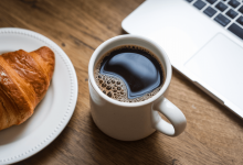 Чашка кави з круасаном та ноутбуком на столі