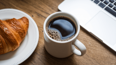 Чашка кави з круасаном та ноутбуком на столі