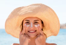 Девушка в пляжной шляпе наносит крем на лицо