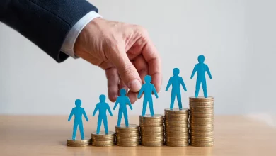 5 стопок монеток та пластикові чоловічки на них і рука людини