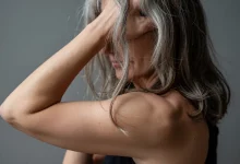 Жінка з сивиною тримає руку у волосся