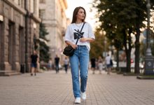 Елегантний літній образ 2026: жінка демонструє модну футболку в повсякденному стилі на фоні міського парку.